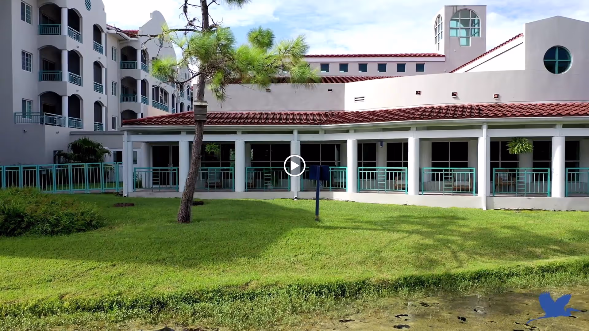 Front exterior of a senior living building with columns, a covered terrace, green lawn and a small pond.