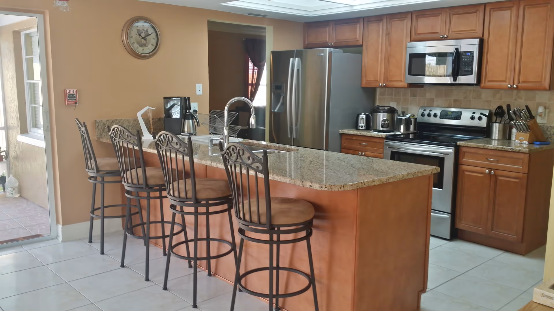 Modern kitchen with a granite island and four bar stools, stainless steel appliances, and wooden cabinets.