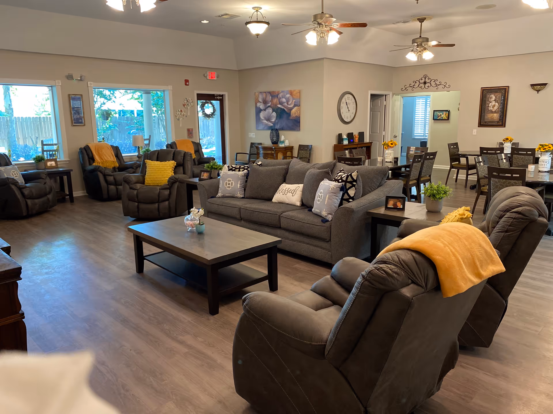 Open common living area with sofas and recliners arranged around a coffee table and dining tables visible in the background.