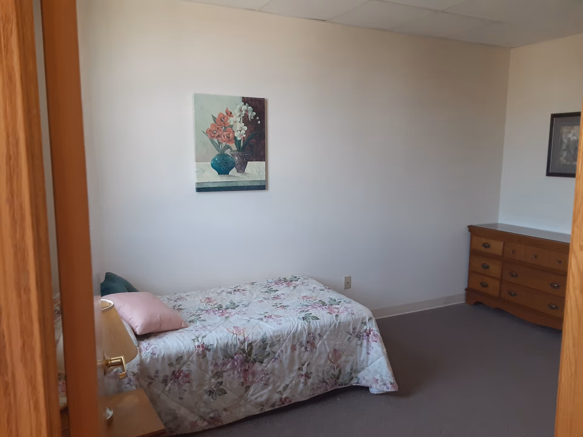 Small bedroom with a single bed covered in floral bedding, a wooden dresser, and wall art.