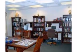 Community library/common room with bookshelves, tables and chairs and computer stations.
