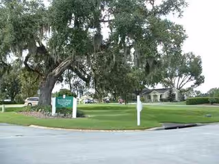 Outdoor view of Pennbrooke Fairways: green lawn, trees, signs, and a building.