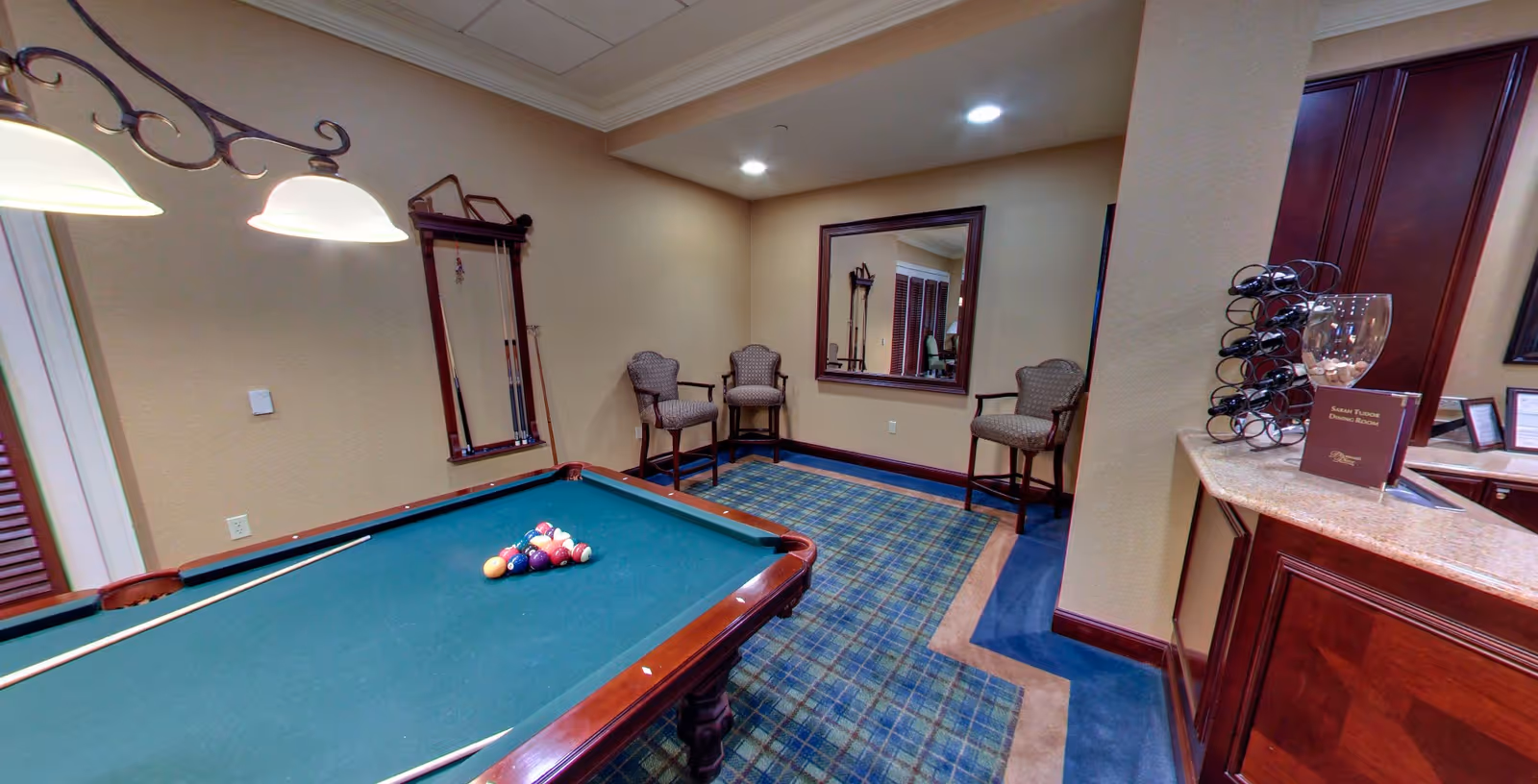Indoor recreation room with a pool table, a set of chairs by a wall mirror, and a countertop with a wine rack.
