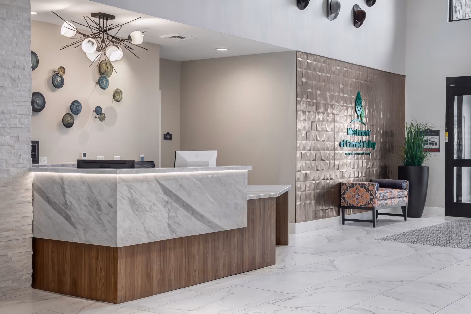 Reception desk and lobby interior featuring a marble countertop, decorative wall art, seating bench, and a 'Westmont of Carmel Valley' sign.