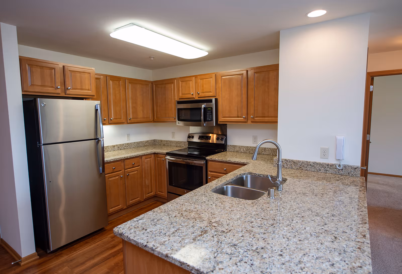 Modern kitchen with granite countertops, stainless steel appliances, wooden cabinets, and a peninsula sink.