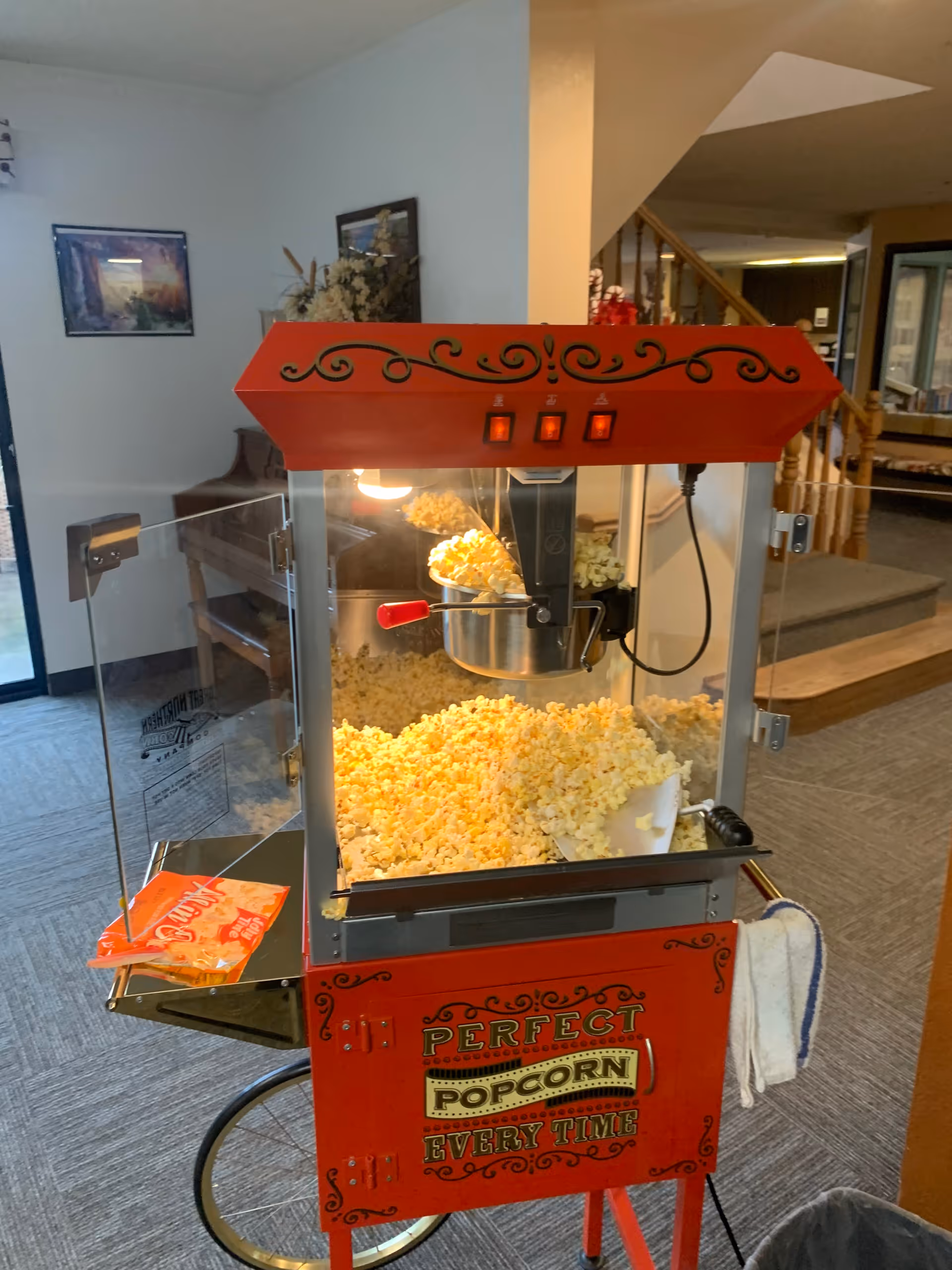 Red vintage-style popcorn machine filled with popcorn set in a communal interior room.