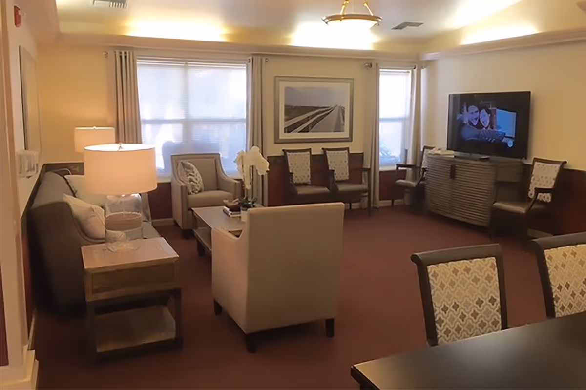 Bright common living room with sofas, armchairs, a coffee table and a television in a senior living facility.