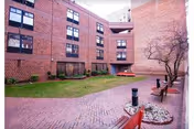 Brick courtyard with benches, a small lawn and walkways surrounded by a multi-story brick building.