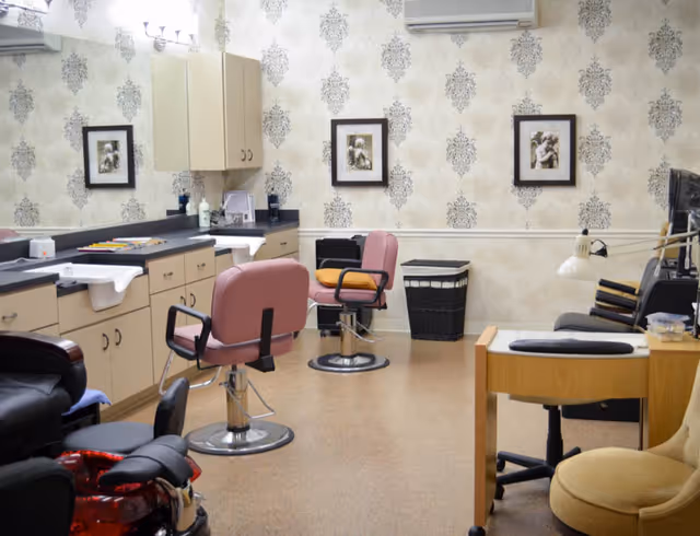 Interior view of a senior living facility hair salon with pink chairs, sinks, and mirrors.