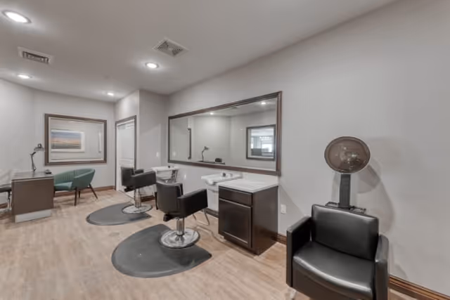 Interior salon area with styling chairs, large mirror, shampoo sink and a hooded hair dryer.