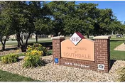 Outdoor view of a brick sign for Southdale Towers with landscaping including rocks, flowers, and trees in the background under a clear sky.