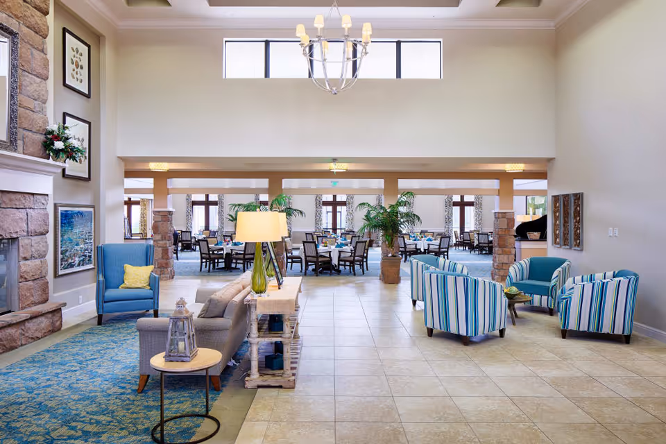 Spacious lobby-style lounge with couches and striped chairs facing a dining area under a chandelier.