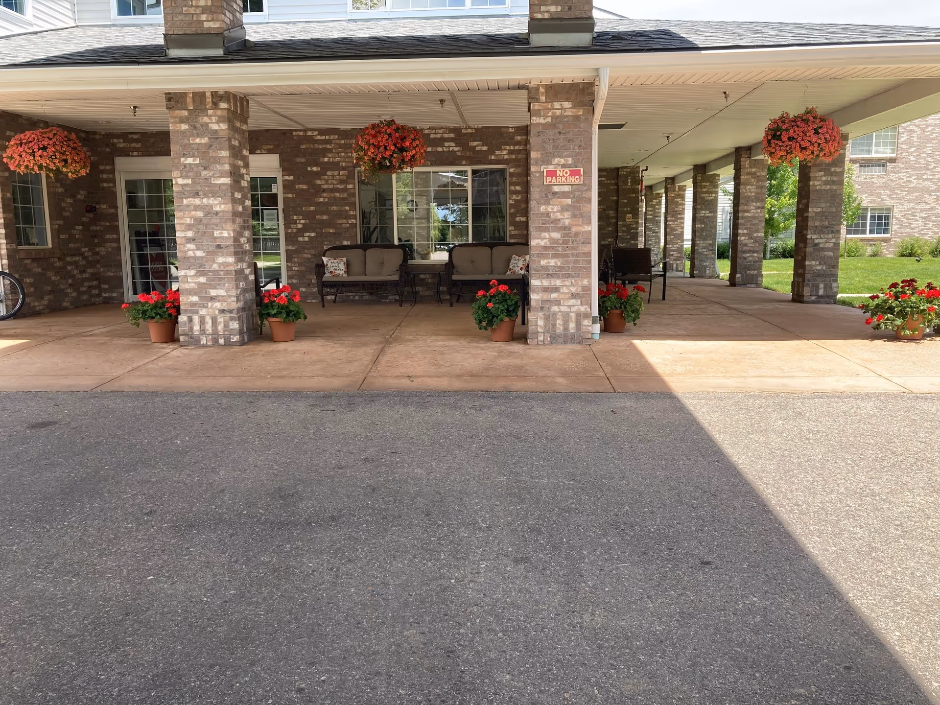 Covered brick entrance with columns, outdoor seating, and hanging flower baskets over a drive-up area.