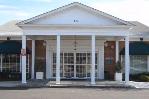 Front entrance of a brick facility with white columns and double glass doors.