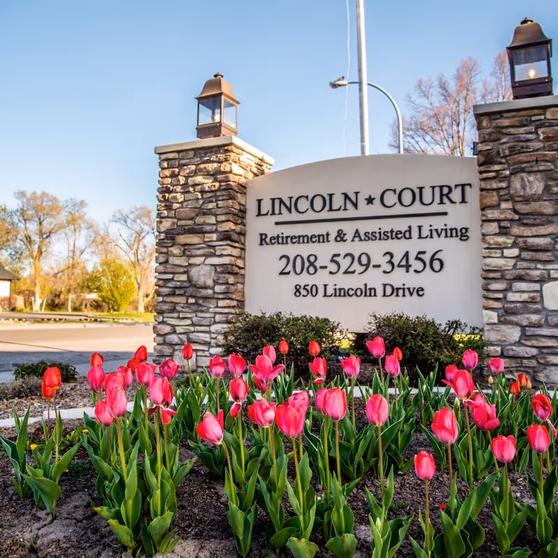 Stone entrance sign for Lincoln Court Retirement & Assisted Living surrounded by pink tulips.