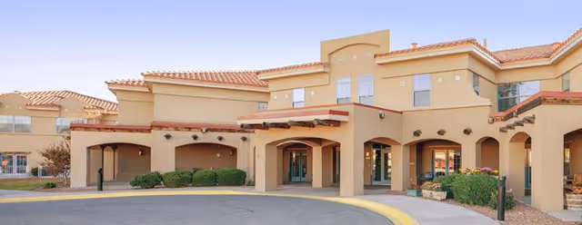 Exterior of The Village at Northrise, a tan stucco senior living facility with arches and entrance.
