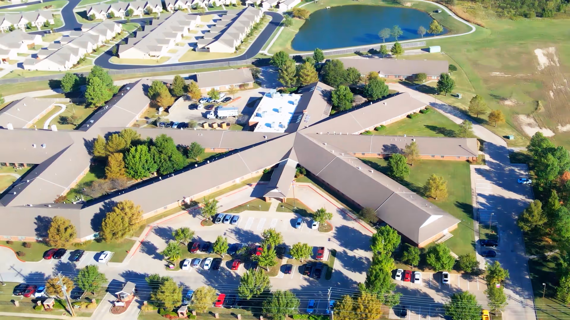 Aerial view of Forest Hills Care and Rehab showing a star-shaped single-story building with multiple wings, surrounding parking lots, trees, and a nearby pond.