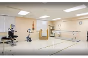 Interior rehabilitation gym with parallel bars, stationary bike, and other therapy equipment.