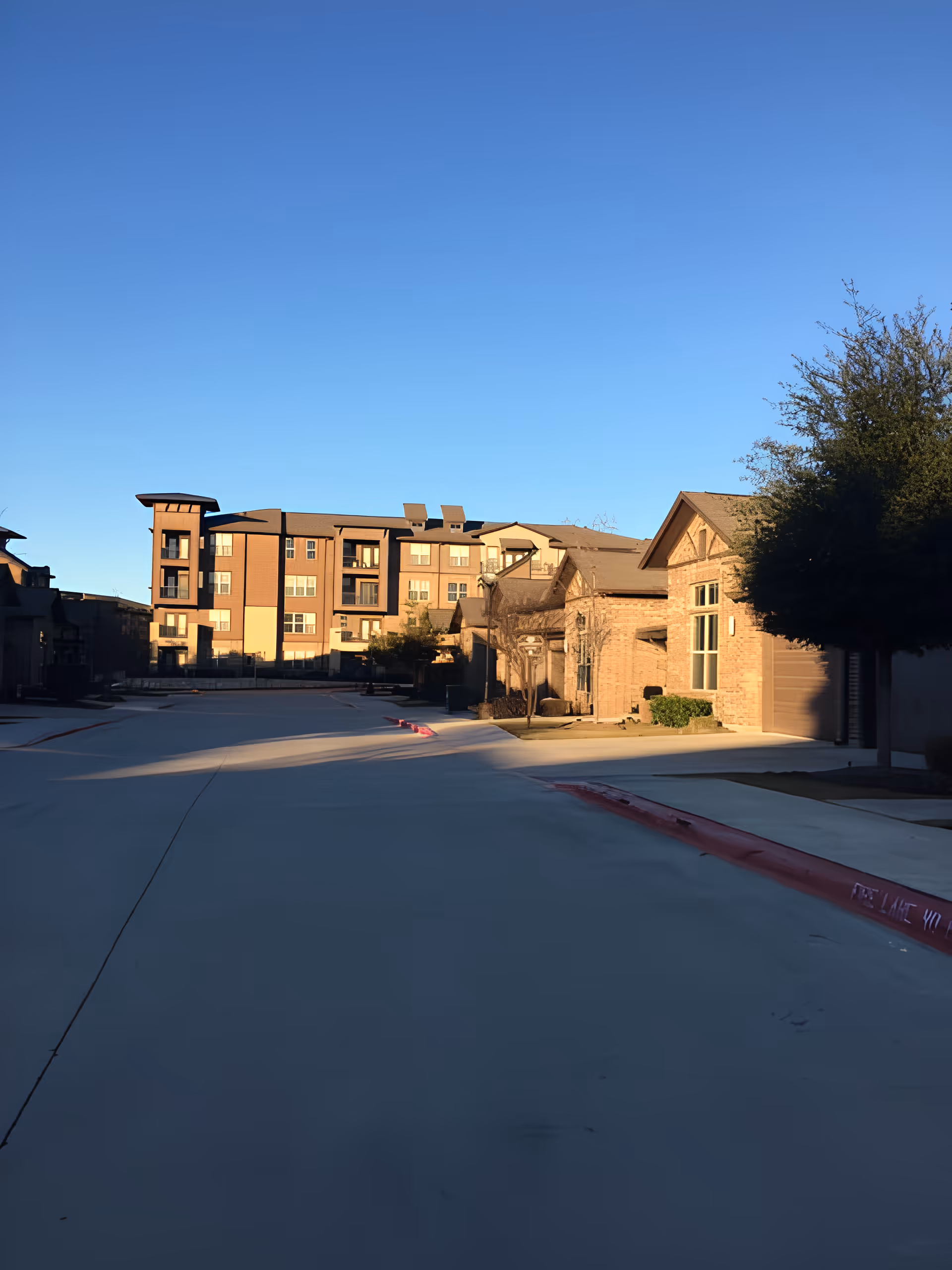 View of a senior living campus showing multi-story and single-story buildings along a wide driveway under a clear blue sky.