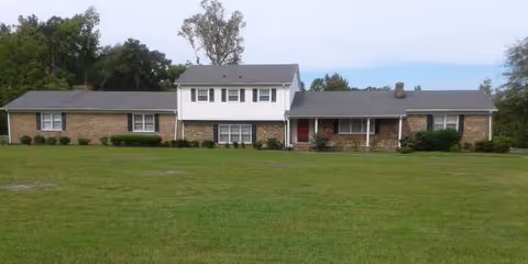 Front view of a brick and white senior living facility with a large green lawn.