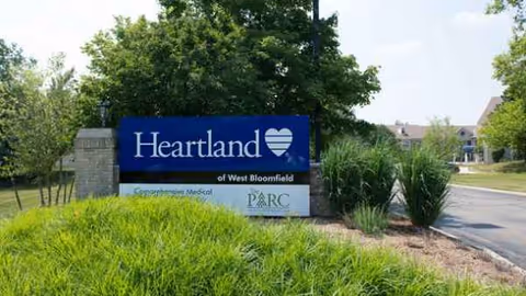 Blue Heartland sign for West Bloomfield facility near entrance, surrounded by landscaping.