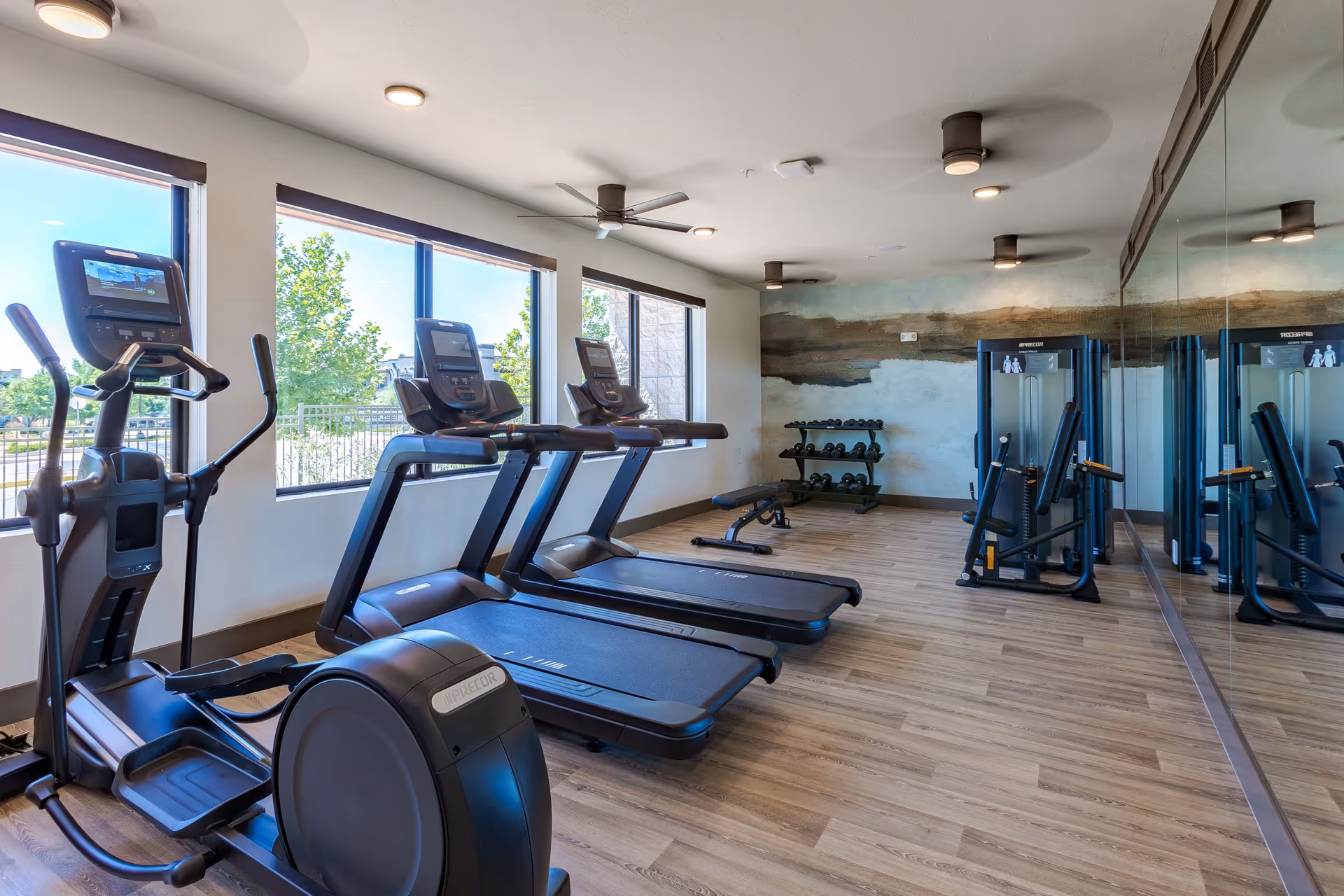 Bright fitness room with treadmills, an elliptical, free weights and a mirrored wall.