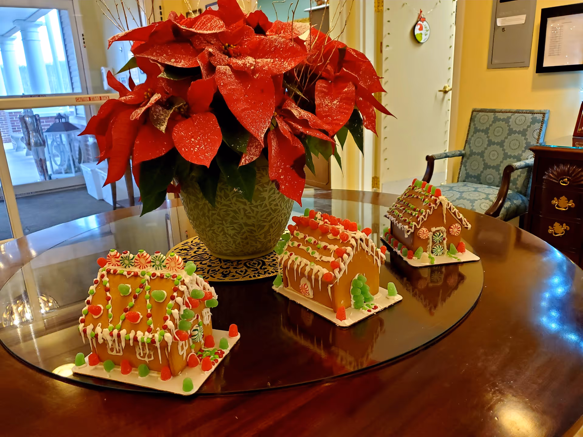 Three decorated gingerbread houses and a poinsettia centerpiece on a round table in a facility lobby.