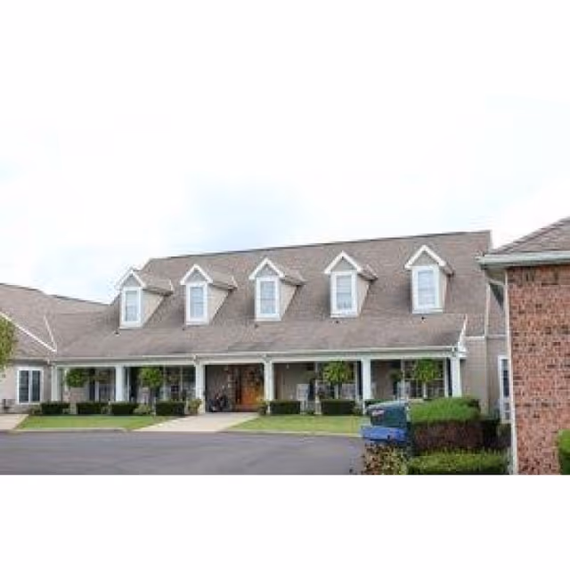 Front exterior of a single-story assisted living building with dormer windows, a covered porch, and landscaped driveway.