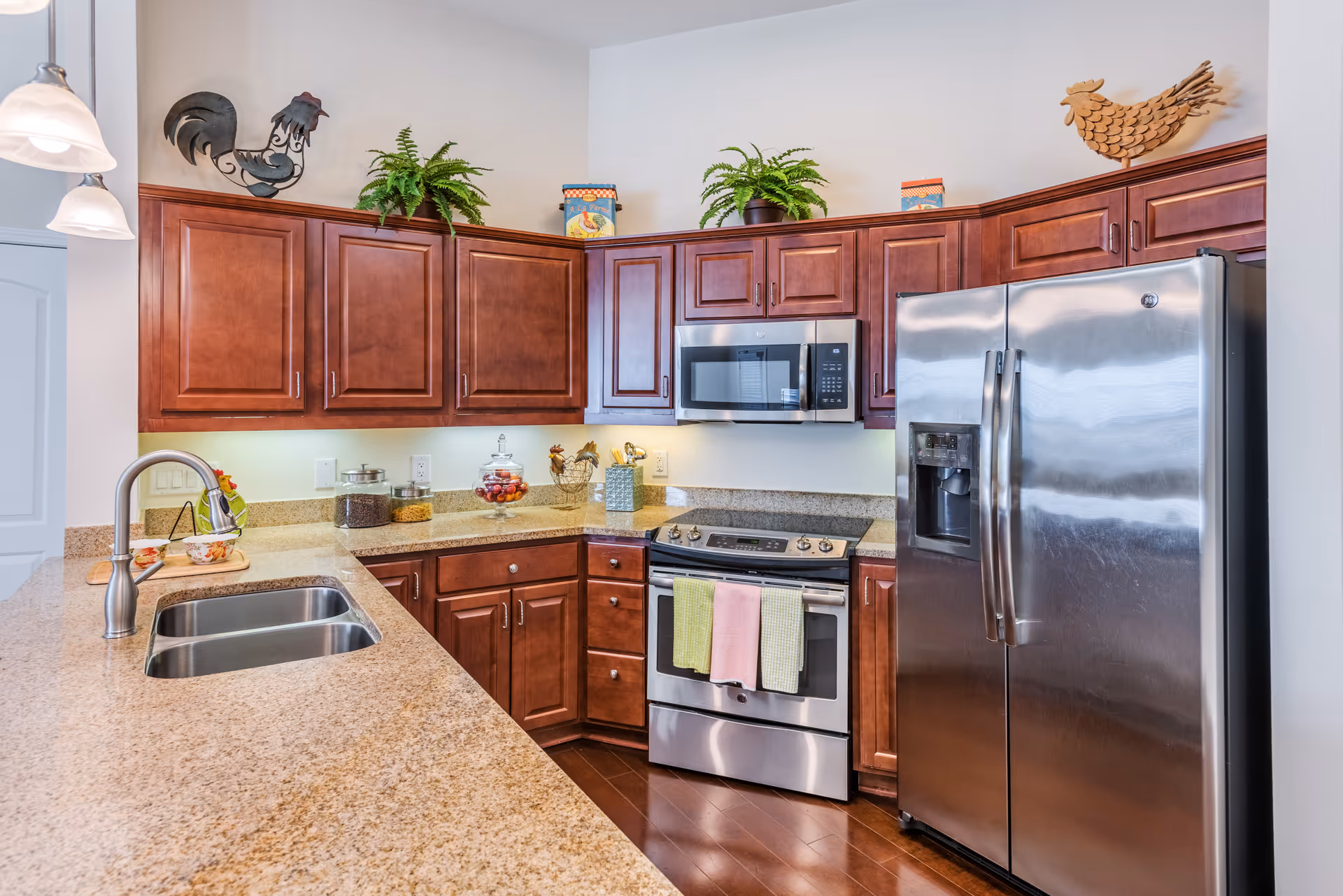 Modern kitchen with granite countertops, a double-basin sink in an island, stainless steel refrigerator and oven, and dark wood cabinets.