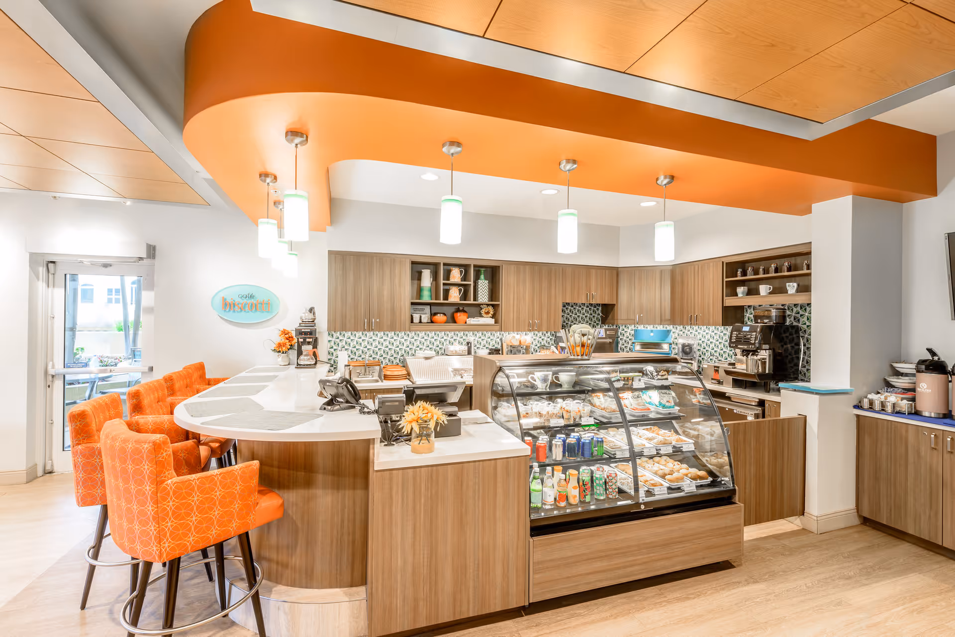 Bright cafe-style serving counter with a glass pastry display, orange barstools, and pendant lights in a modern dining area.