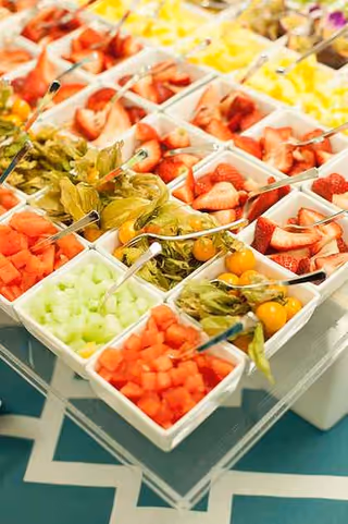 Assorted fresh fruit and salads displayed in white bowls at a buffet.