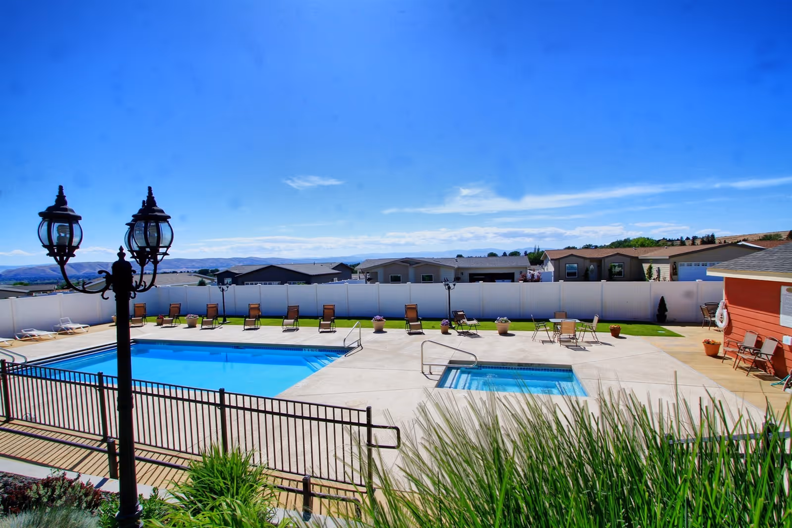 Outdoor swimming pool area at Quail Run facility with lounge chairs arranged along the poolside, a hot tub adjacent to the pool, a white privacy fence surrounding the area, and a clear blue sky overhead.
