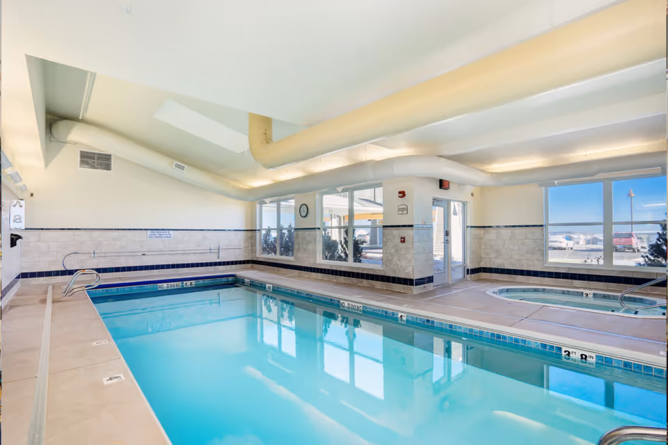Indoor swimming pool and adjacent hot tub in a bright recreation room with large windows.