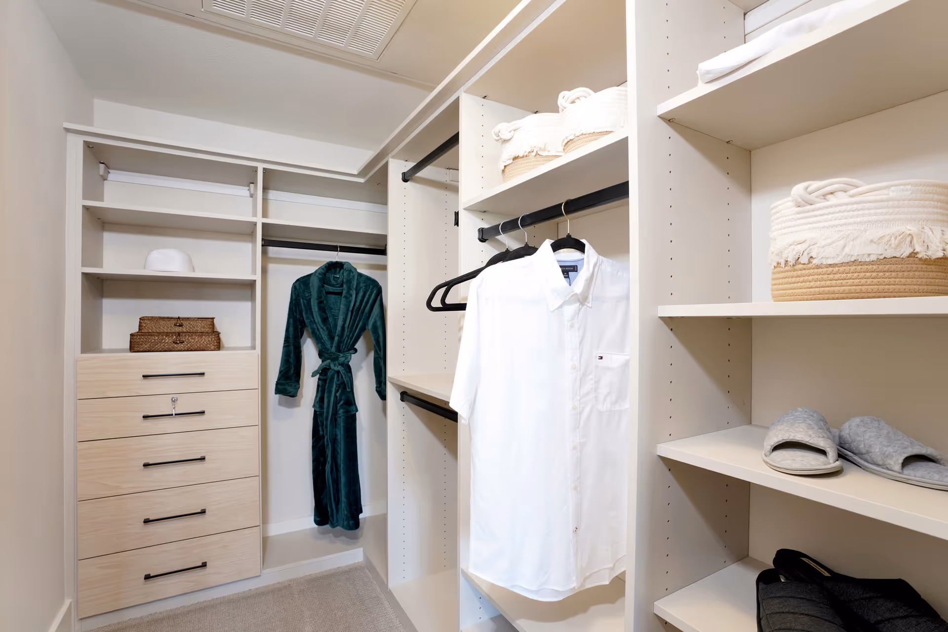 Well-organized walk-in closet with built-in shelves and drawers, a hanging green robe and white shirt, baskets and slippers.