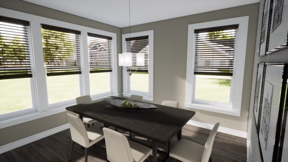 A bright dining room with a dark wooden rectangular table surrounded by six beige upholstered chairs. The room has multiple large windows with dark blinds partially open, allowing natural light to fill the space. A modern pendant light hangs above the table, and framed artwork is visible on the wall to the right.