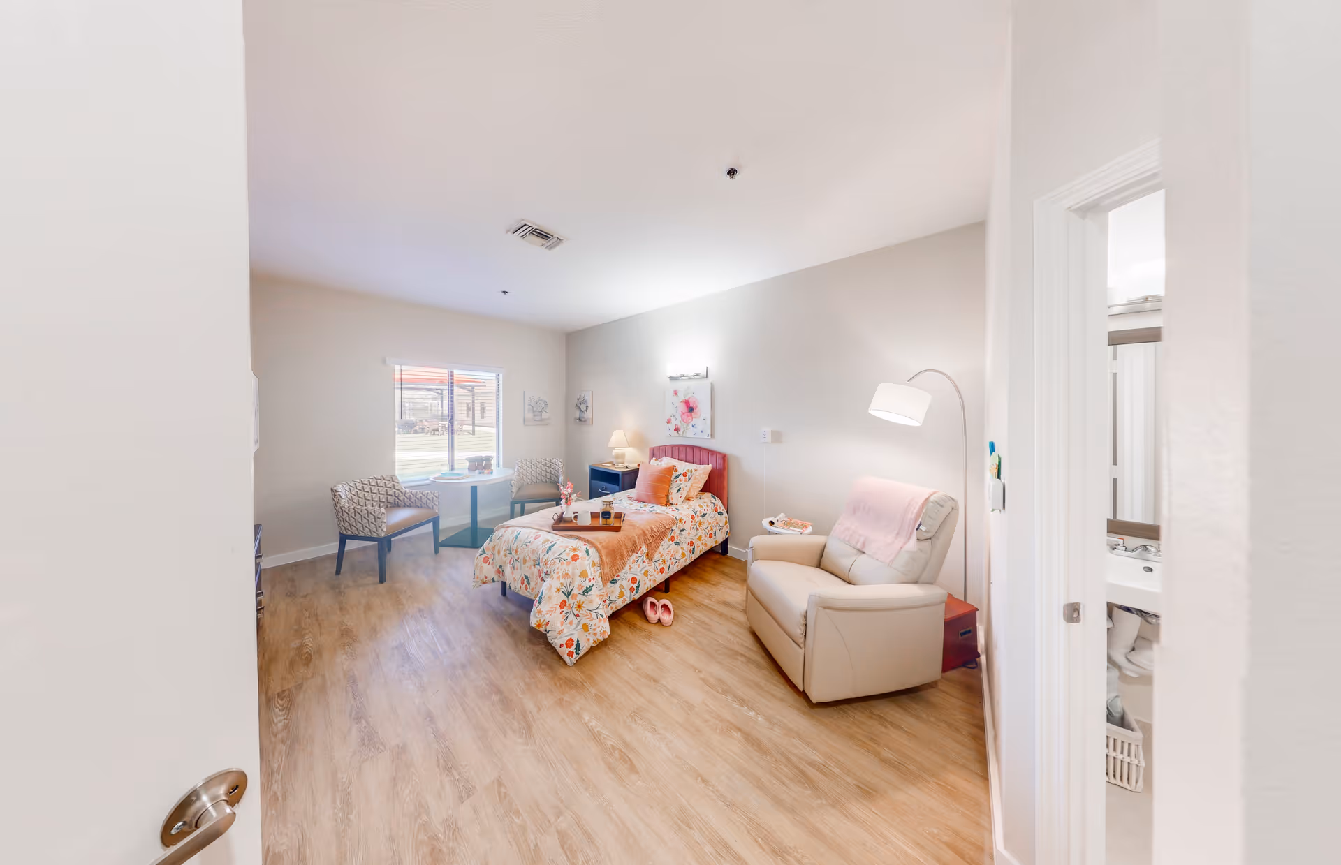 Bright senior living private bedroom with a single bed, recliner, and seating area by a window.
