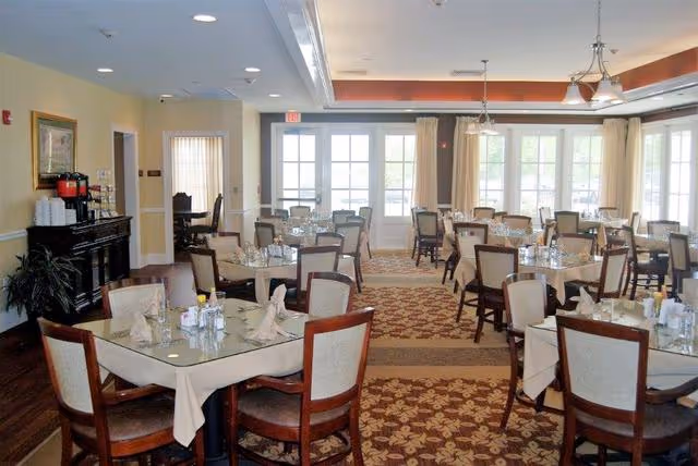 Dining room with multiple set tables and chairs, chandeliers, and large windows.
