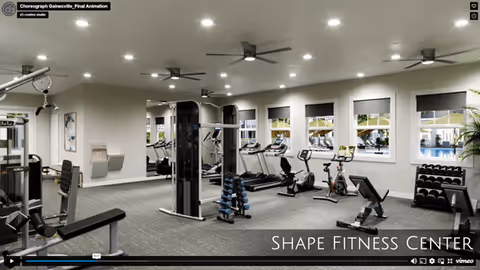 Interior view of a fitness center with various exercise equipment including treadmills, stationary bikes, weight machines, dumbbells, and benches. The room has multiple windows with roller shades, ceiling fans, and recessed lighting.