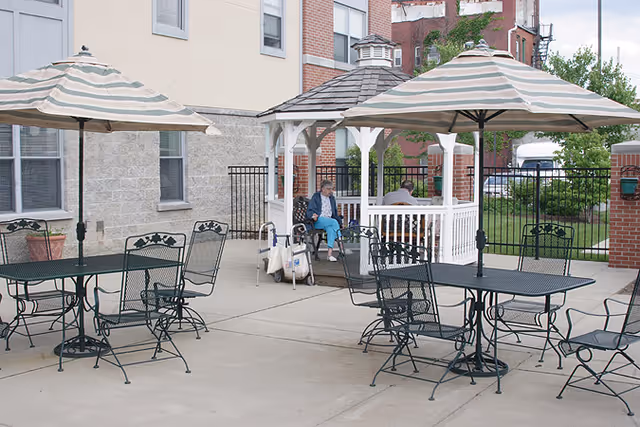 Outdoor patio with metal tables and umbrellas and a white gazebo where two older adults sit.