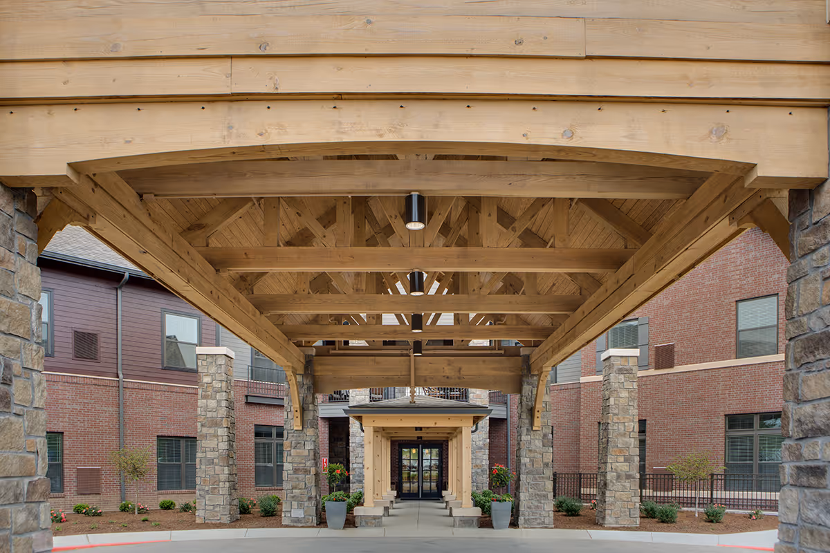 Covered wooden porte-cochere entrance with stone pillars leading to the brick facade of the building.