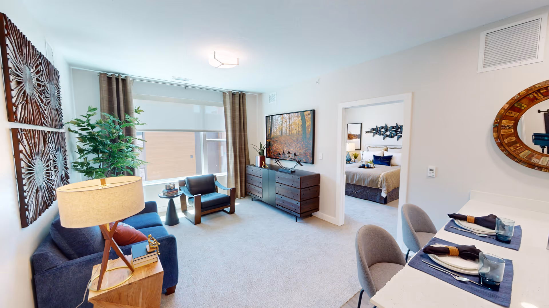 Bright open living room with a sofa, armchairs, dresser and counter dining set, looking into a bedroom.
