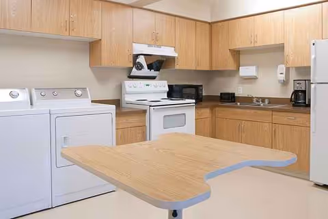 Shared facility kitchen with wooden cabinets, appliances, washer/dryer, and a foldable table.