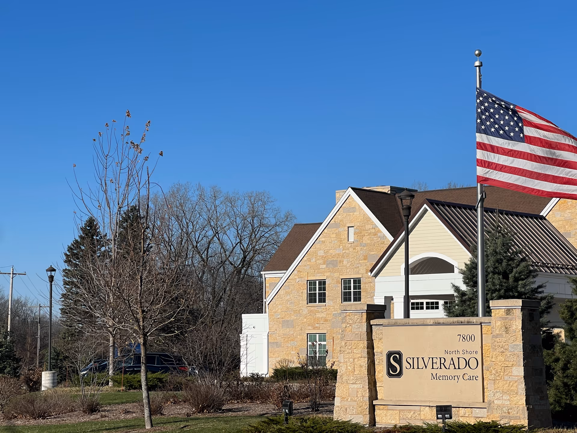 Exterior view of a stone Silverado Memory Care building with an American flag and a sign reading "Silverado Memory Care".