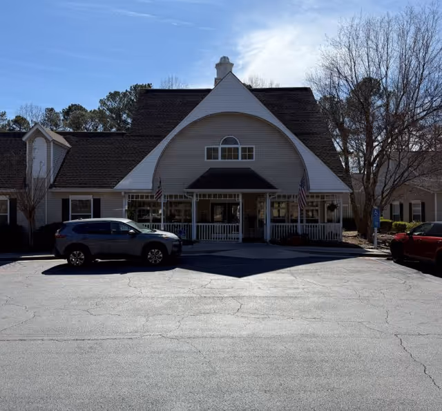 Front exterior of a senior living community building with a covered entrance and parked cars.