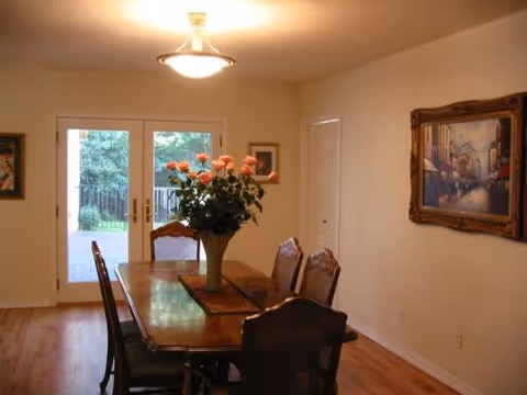 Dining room with wooden table, chairs, vase of flowers, and glass doors.