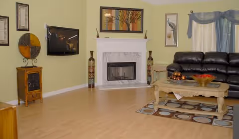 Spacious living room with a fireplace, wall-mounted TV, black leather sofa and a coffee table on a rug.