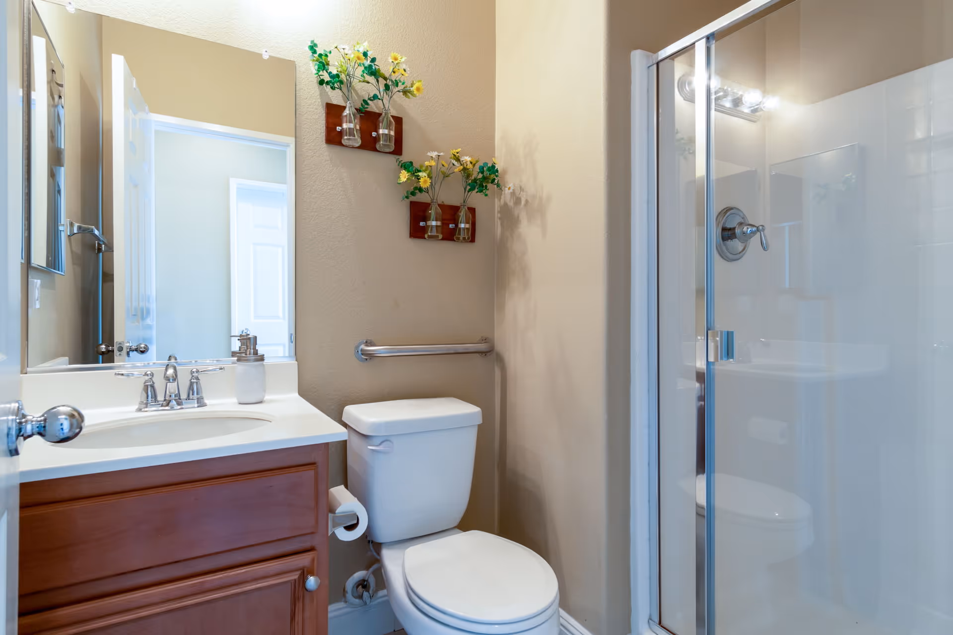Small bathroom with a vanity sink and mirror, a toilet beside a glass-enclosed shower, and wall-mounted floral decorations.