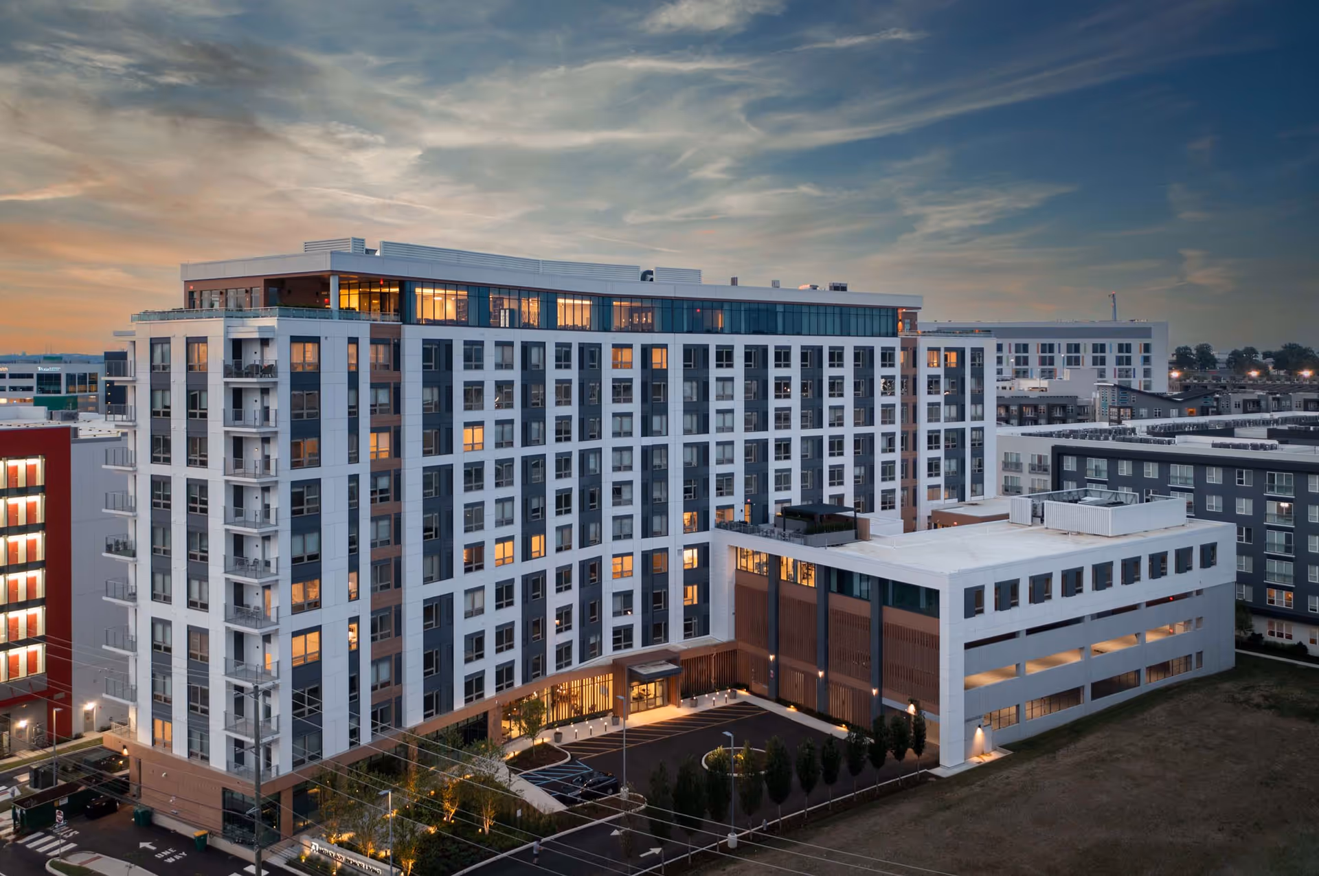 Aerial view of a large modern senior living building with multiple stories and balconies at dusk.