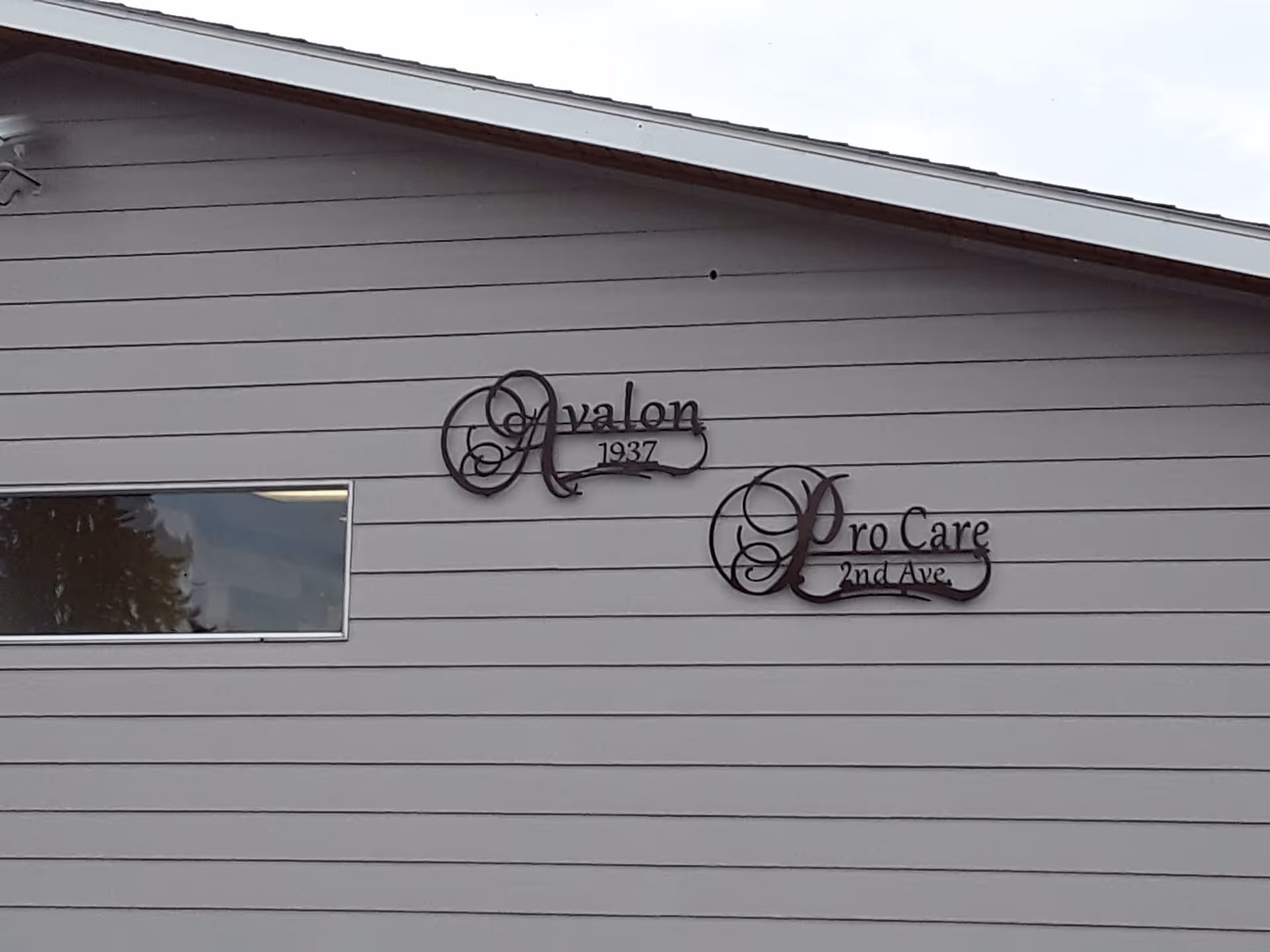 Exterior siding of a building displaying decorative metal signs reading 'Avalon 1937' and 'Pro Care 2nd Ave.'