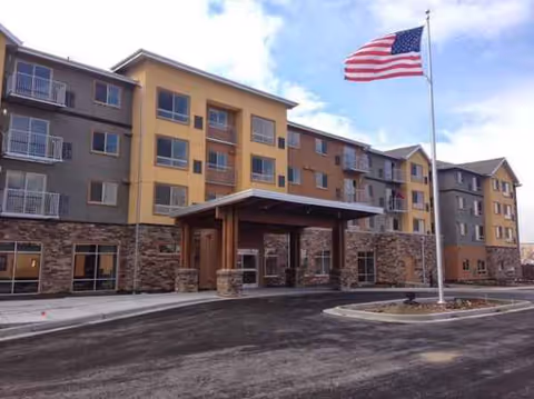 Three-story senior living building with stone base, entrance canopy, and American flag.